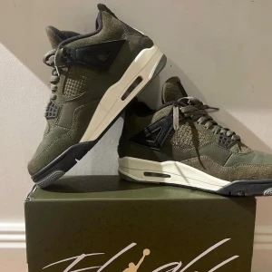 Nike Jordan 4 Olive sneakers - Säljer ett par Nike Jordan 4 sneakers i olivgrönt med svarta och vita detaljer. Skorna har en chunky siluett, meshpaneler och snörning. Materialmix av mocka och syntet ger en cool textur. Ikonisk Jumpman-logga på plösen och platt sula med luftdämpning.