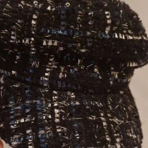 Svart rutig keps med glittriga detaljer - Snygg svart keps med rutigt mönster och glittriga inslag i blått och silver. Materialet är grovt vävt med insydda trådar som ger en cool textur och extra bling. Perfekt för dig som vill sticka ut med en unik accessoar.