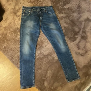 Levi's 511 blå jeans skinny fit - Säljer ett par klassiska Levi's 511 jeans i blå tvätt med snygga slitningar. Modellen har skinny fit och normal midja, fem fickor och dragkedja. Perfekta för dig som gillar en smal siluett och tidlös denimstil.