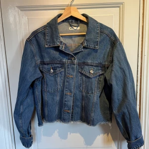 Blå croppad jeansjacka från Gina Tricot - Säljer en blå croppad jeansjacka från Gina Tricot med rå kant nertill, klassisk krage och bröstfickor med knappar. Jackan har en loose passform och långa ärmar. Perfekt att slänga över en hoodie eller t-shirt. Jag är normalt stl xs 