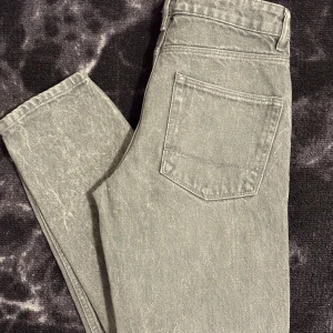 Grå jeansbyxor med knappar - Säljer ett par grå jeansbyxor med klassisk femficksdesign och knäppning framtill. Byxorna har raka ben och är tillverkade i ett slitstarkt jeanstyg. Perfekta för dig som gillar en enkel och stilren look.