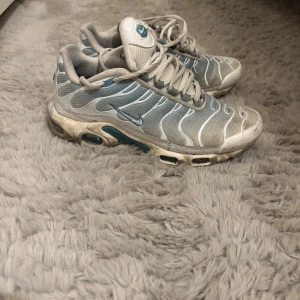 Nike Air Max Plus Tn sneakers grå/blå - Nike Air Max Plus Tn sneakers i grått och blått med vita detaljer. Skorna har mesh- och syntetmaterial, ikoniska vågformade linjer och synlig Air Max-dämpning i sulan. Tn-logga bak och snörning framtill. Perfekta för dig som gillar streetwear och sportig stil. En av Nike märket har fursvunnit och det är lite trasiga ränder.