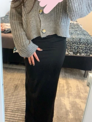 Svart långkjol med slits - Snygg svart långkjol med slits på sidan. Kjolen har en tight passform och är gjord i ett stretchigt material som sitter skönt på kroppen i storlek XS/S