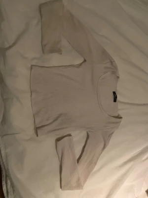 Ljusribbad långärmad topp från New Yorker  - Säljer en ljus, ribbad långärmad topp från New Yorker. Toppen har en rund halsringning och är croppad i modellen, vilket ger en trendig look. Perfekt att matcha med höga jeans eller kjol.