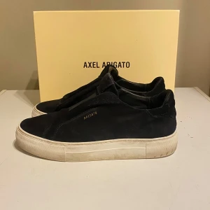 Svarta sneakers från Axel Arigato - Stilrena svarta sneakers från Axel Arigato i mocka med diskret guldfärgad logga på sidan. Skorna har en klassisk låg siluett och vit, tjock gummisula. Perfekta för dig som gillar minimalistisk och clean design. Hör av dig direkt om du har någon fråga, jag har köpt dem på ni finns kvitto, man får med box dustbag  nypriss 2599kr Dem passar 40. Priset är inte hugget i sten snabb affär kan gå ner.  SVARAR SNABBT 