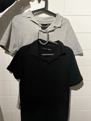 Svart och grå pikétröja (2 for 1) - Två klassiska pikétröjor från lager157 en i svart och en i ljusgrått. Båda har krage, korta ärmar och knappar vid halsen. Perfekta för en stilren och enkel look.