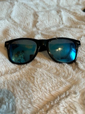 Svarta solglasögon med blå spegelglas - Snygga solglasögon med svart båge och blå spegelglas. Klassisk fyrkantig form som ger en cool look. Perfekta för soliga dagar och att lyfta din stil.