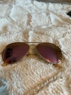 Guldiga aviator solglasögon - Snygga aviator solglasögon med guldfärgad metallbåge och rosatonade spegelglas. Klassisk pilotmodell som ger en cool och trendig look. Perfekta för soliga dagar och passar till de flesta outfits.