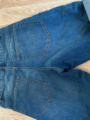 Blå denimshorts med uppvik - Säljer ett par klassiska blå jeansshorts sopassade med uppvikta benslut och femficksmodell. Shortsen har bälteshällor och stängs med dragkedja och knapp. Perfekta för sommardagar och enkla att matcha med allt.