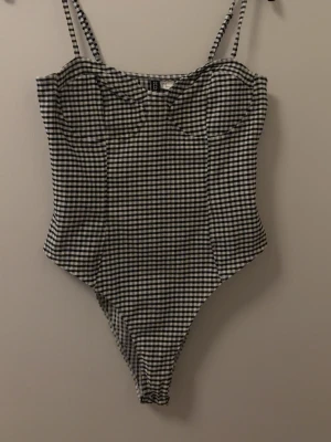 Rutig body från H&M Divided - Snygg body med svartvitt rutmönster från H&M Divided. Modellen har tunna axelband och markerade sömmar vid bysten för en schysst passform. Perfekt att styla med jeans eller kjol. 