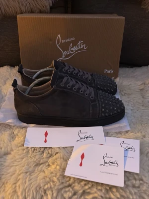 Svarta Christian Louboutin sneakers - Snygga svarta sneakers från Christian Louboutin i mocka med svarta nitar på tån. Klassisk låg modell med svarta skosnören och sula. Perfekta för dig som vill sticka ut med exklusiv design och edgy detaljer. Låda och care instructions medföljer (allt på bilderna). 