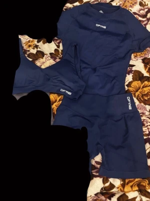 Mörkblått träningsset från DFYNE - Snyggt mörkblått träningsset från DFYNE med kortärmad topp, sport-bh och shorts. Setet är tillverkat i ett stretchigt funktionsmaterial som andas, perfekt för gym eller löpning. Diskret logga på alla delar för en clean look.
