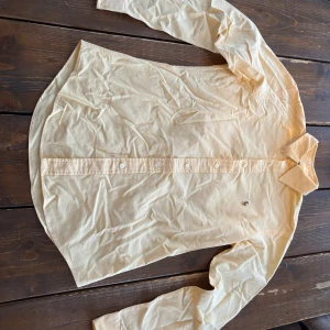 Gul skjorta från Ralph Lauren - Klassisk gul skjorta från Ralph Lauren med lång ärm och knappar framtill. Skjortan har en liten broderad logga på bröstet och är tillverkad i mjuk sopm bomull. Perfekt till en avslappnad men ändå stilren look.