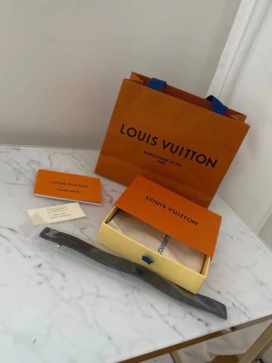 Louis Vuitton svart armband - Snyggt svart armband från Louis Vuitton med det klassiska LV-märket i silver på framsidan. Armbandet har en stilren och modern design och kommer i originalförpackning med tillhörande påse och certifikat. Perfekt accessoar för dig som gillar exklusiva detaljer.