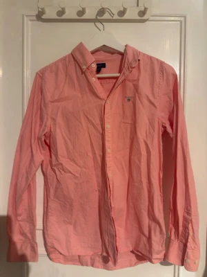 Rosa skjorta från Gant i bomull - Klassisk rosa skjorta från Gant med button-down krage och broderad logga på bröstet. Skjortan har långa ärmar, vita knappar och är tillverkad i mjuk bomull. Perfekt för en avslappnad men ändå stilren look.