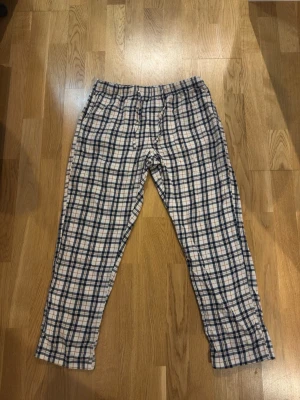 Rutiga pyjamasbyxor i bomull - Mysiga pyjamasbyxor med klassiskt rutmönster i vitt, blått och beige. Byxorna har resår i midjan och raka ben, perfekta för chillkvällar hemma. Tillverkade i mjuk bomull som känns skön mot huden.