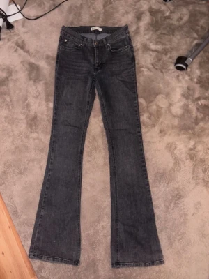 Mörkgrå lowrise bootcut jeans från Gina Tricot - Säljer ett par mörkgrå bootcut jeans med klassisk femficksdesign och knappgylf. Jeansen har låg midja och raka ben som går ut i en lätt utsvängd form. Perfekta för en avslappnad men ändå snygg look.