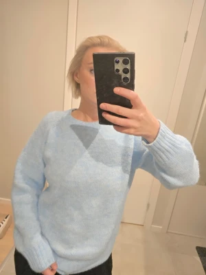 Ljusblå stickad tröja 100% mohair - Mysig ljusblå stickad tröja med rund hals och långa ärmar. Tröjan har ribbstickade muddar vid ärmslut och nederkant, vilket ger en skön passform. Perfekt för att hålla sig varm under kyliga dagar. Materialet är 100% mohair