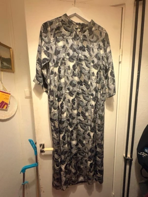 Svartvit skjortklänning med bladmönster - Svartvit skjortklänning från Bckenna med bladmönster. Klänningen har korta ärmar, knappar framtill och en rak, loose passform. Perfekt för dig som gillar unika mönster och avslappnad stil. Är aldrig använd. Jag fick den i en MollyandMy goodiebag men är inte min still. Den är i storlek S/M. 