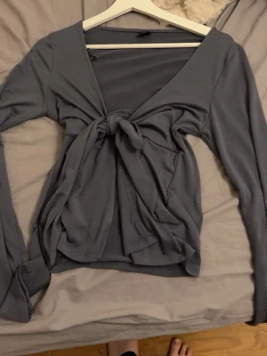 Grå omlottopp med knyt framtill - Trendig grå omlottopp med långa ärmar och snygg knytning framtill. Djup v-ringning ger en modern look och mjukt bomullsliknande material gör den bekväm att bära. Perfekt att styla med jeans eller kjol för en cool outfit.