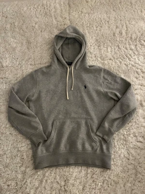 Grå hoodie från Polo Ralph Lauren - Klassisk grå hoodie från Polo Ralph Lauren. Storlek S. Fint skick, finns bara en liten skada vid handleden ( sista bilden)
