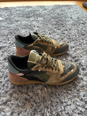 Valentino rockrunners - Snygga sneakers från Valentino med camomönster i grönt, beige och svart. Skorna har detaljer i mocka och läder samt en unik häl i brunt med nitar. Klassisk låg modell med gröna skosnören och logga på plösen. 