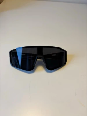 Svarat Pit Viper liknande - Snygga svarta solglasögon med sportig och futuristisk design. De har stora, rektangulära linser och bred båge som ger en cool look. Perfekta för dig som gillar en modern stil och vill sticka ut. Lätta och bekväma att bära.