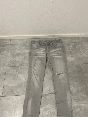 Grå slitna disqred2 med qr kod - Säljer ett par grå skinny jeans från disqred med slitningar och hål på flera ställen för en trendig, avslappnad look. Jeansen har klassisk femficksmodell och knappgylf. Perfekta för dig som gillar streetstyle och vill ha en edgy vibe.