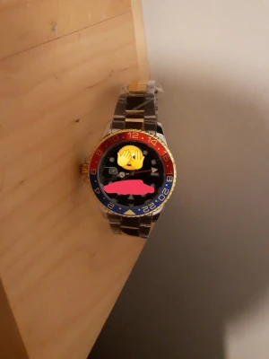 Färgstark klocka med metallarmband - Snygg klocka med tvåfärgad vridring i rött och blått, svart urtavla och detaljer i guld. Armbandet är i metall med både silver- och guldfärgade länkar.