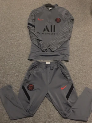 Grå PSG träningsset från Nike.Strolek M pris kan diskuteras - Snyggt psg kit storlek M på byxor och tröjan. Byxorna har dragkedja vid slutet av benet. Funkar bra för träning riktigt sköna byxor. Byxorna  passar nog bäst för 1,70-1,80. Tröjan funkar bra upp till 1,85 skulle jag säga. Pris går att diskutera vid snabbt köp. Skickar iväg mellan 1-2 dagar👍