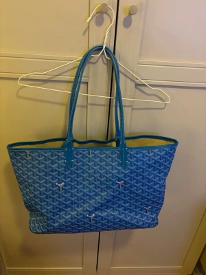 Blå shoppingväska  - Säljer en ikonisk blå shoppingväska med långa handtag. Väskan är rymlig och har beige insida samt detaljer i blått. Perfekt för dig som vill ha en statement bag med plats för allt du behöver. Har en fläck på insidan som jag inte testat ta bort!