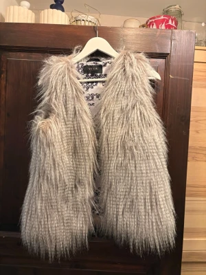 Ljusgrå långhårig pälsväst VILA - Säljer en fluffig och långhårig pälsväst från VILA i ljusgrå nyans. Den är nästan helt ny, Västen har öppen front och ett coolt, trendigt uttryck med sitt långa fuskpälsmaterial. Perfekt för att lyfta vilken outfit som helst.