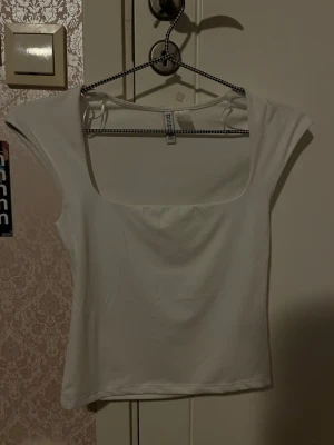 Vit croppad topp från Divided - Säljer en vit croppad topp från Divided med fyrkantig ringning och korta ärmar. Enkel och stilren design som passar perfekt till jeans eller kjol. Tunn och mjuk i materialet.