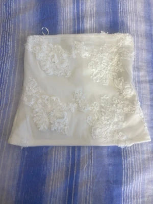 Vit spets bandeau tubtopp - Säljer en vit bandeau tubtopp med vackra spetsdetaljer och broderade blommor. Toppen är axelbandslös och har en romantisk känsla, perfekt för sommarens alla tillfällen. Passar dig som gillar en feminin och trendig stil.