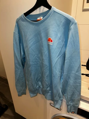 Ljusblå sweatshirt från Ellesse - Snygg ljusblå sweatshirt från Ellesse med rund halsringning och broderad logga på bröstet. Tröjan är i storlek L men passar också M. Tröjan har långa ärmar och ribbade muddar vid ärmslut och nederkant. Perfekt för en avslappnad och sportig stil. Skriv över det minsta lilla eller över den minsta funderingen!🔥🔥