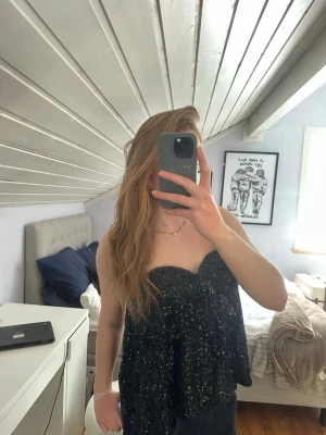 Svart glittrig topp - Säljer en svart glittrig bandeau topp. Toppen är axelbandslös och flowy i passformen! Perfekt till utekvällar eller fester💕endast använd två gånger och i väldigt bra skick