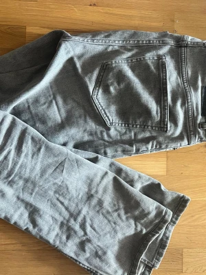 Grå raka jeans med hög midja - Säljer ett par grå jeans med rak passform och hög midja. Jeansen har klassiska bakfickor och är tillverkade i ett mjukt denimtyg. Perfekta för en avslappnad och trendig look.