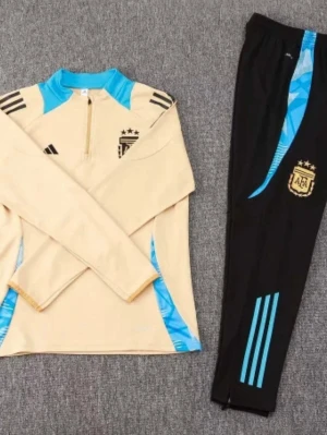 Argentina träningsset från Adidas - Snyggt träningsset från Adidas med Argentina-tema. Tröjan är beige med ljusblå detaljer, halv dragkedja och svarta ränder på axlarna. Byxorna är svarta med ljusblå ränder och Argentina-logga. Perfekt för fotbollsträning eller chill.