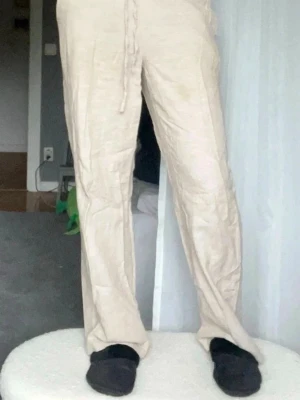 Beiga linnebyxor med dragsko - Säljer ett par snygga beiga linnebyxor med avslappnad passform och dragsko i midjan. Byxorna har raka ben och är tillverkade i ett lätt och luftigt linnematerial.
