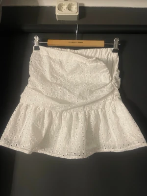 Vit sommarkjol - Supersöt vit kortkjol med broderade blommönster och volangkant. Kjolen har omlottkänsla och dragkedja i sidan för enkel på- och avtagning. Aldrig Använd. Perfekt för sommarens alla tillfällen! 🤍