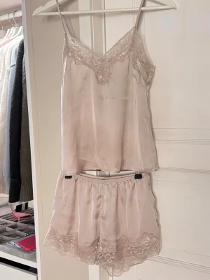 Rosa/beige satinpyjamas med spetsdetaljer - Tvådelat pyjamassett från H&M med linne och shorts i spets. Endast testat! De är den färgen som plockats bort så finns inte kvar i sortimentet längre💕Skriv vid frågor