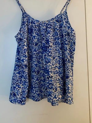 Blåvit mönstrad linnetopp - Säljer en blåvit linnetopp från Lager 157 med tunna axelband och ett unikt mönster. Toppen är luftig och perfekt för varma dagar, med en lös passform som ger en avslappnad vibe. Materialet känns lätt och bekvämt mot huden.