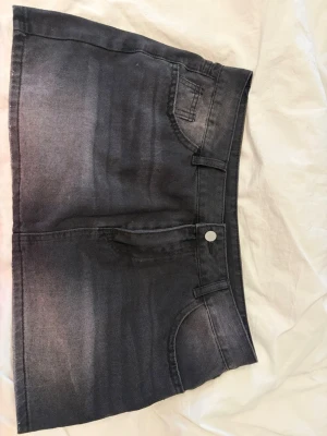 Svart jeanskjol i kort modell - Köpte i en marknad i Spanien så inget märke. Den är kort och lågmidjad skulle behållt men behöver tyvärr pengarna 🥹 Säljer en svart kort jeanskjol med klassisk femficksdesign och knappstängning fram. Kjolen har en rak passform och är perfekt för dig som gillar en enkel men snygg stil. Passar till det mesta och är lätt att matcha med olika toppar.