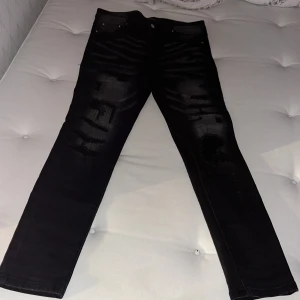 Svarta skinny jeans från Amiri - Svarta jeans från Amiri med skinny passform och slitna detaljer framtill. Jeansen har en cool tvätt med blekta partier och klassiska fem fickor. Materialet är jeans med stretch för extra komfort. Perfekt för dig som gillar streetstyle och edgy look.