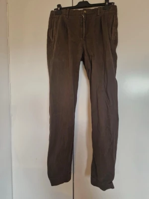 Bruna chinos från Hackett London - Snygga bruna chinos från Hackett London i rak modell. Tillverkade i 99% bomull och 1% elastan för en bekväm och stretchig känsla. Klassisk design med fickor fram och bak, perfekta till en avslappnad men stilren look.