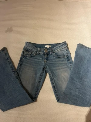 Ljusblå bootcut jeans från Gina Tricot - Snygga ljusblå bootcut jeans från Gina Tricot med klassisk femficksdesign och dubbla knappar i midjan. Jeansen har en lätt tvättad look och raka ben. Perfekta för en avslappnad och trendig stil.