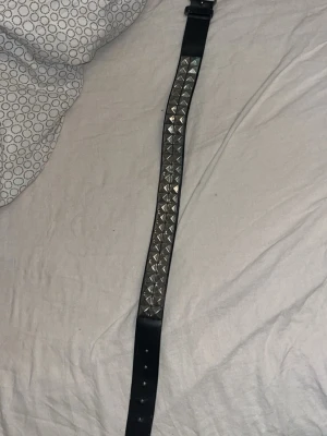Svart nitar bälte i skinn - Säljer ett svart bälte med silverfärgade fyrkantiga nitar. Bältet är gjort i skinn och har ett coolt, edgy uttryck som passar perfekt till jeans eller kjol. Justerbar längd med flera hål för spännet. 65cm långt 