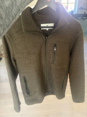 Mörk grön fleecejacka från John Henric (vår jacka) - Mysig brun fleecejacka från John Henric med hel dragkedja, hög krage och tre praktiska fickor med dragkedja. Perfekt för lager-på-lager och chill dagar. Materialet är mjukt och värmande, och jackan har en stilren look.