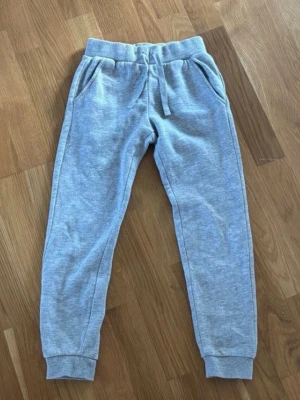 Grå mjukisbyxor med dragsko - Säljer ett par klassiska grå mjukisbyxor med resår i midjan och dragsko. Byxorna har två sidofickor och muddar vid bensluten. Perfekta för chill dagar eller när du vill vara extra bekväm. Materialet känns mjukt och skönt mot huden.