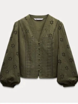 Olivgrön blus med broderade detaljer - Trendig olivgrön blus från Zara med v-ringning och dekorativa knappar framtill. Blusen har broderade blommönster och vida långärmar med resår vid ärmslut. Tillverkad i ett lätt bomullstyg som ger en luftig känsla och snygg passform.